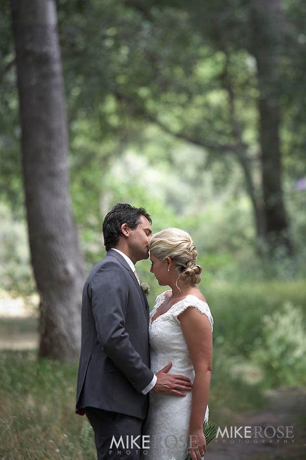 A bride and groom are kissing in the woods.