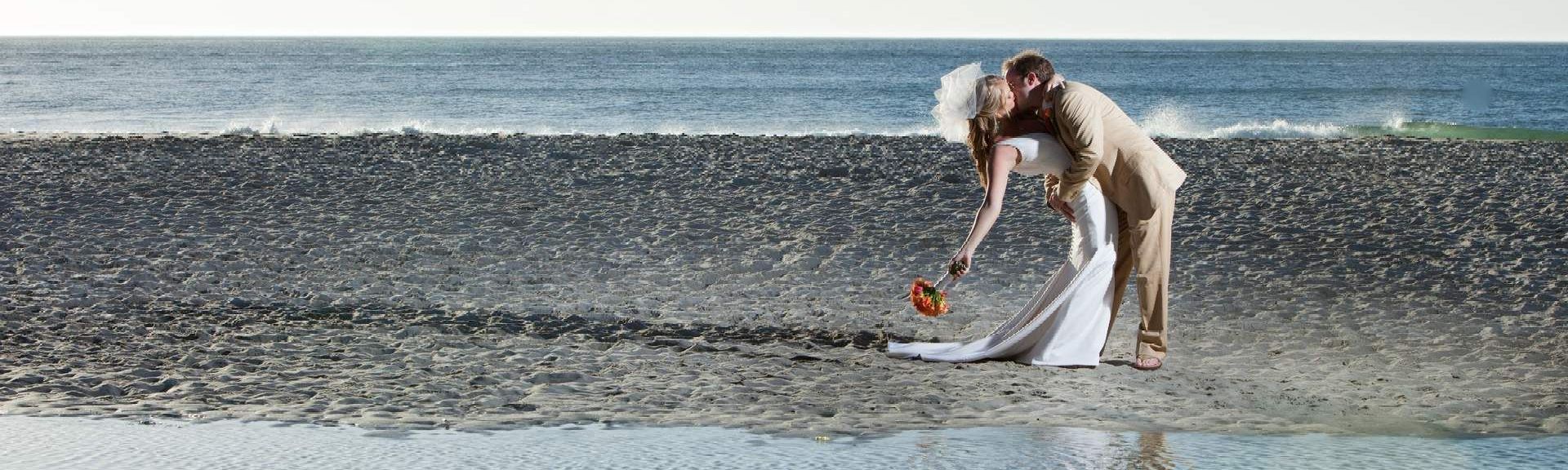 A bride and groom are standing on a beach near the ocean.