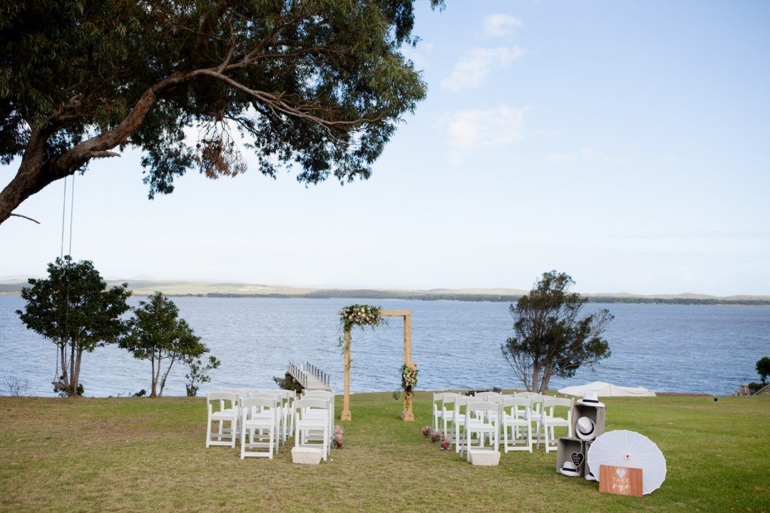 A wedding ceremony is taking place on the shore of a lake.