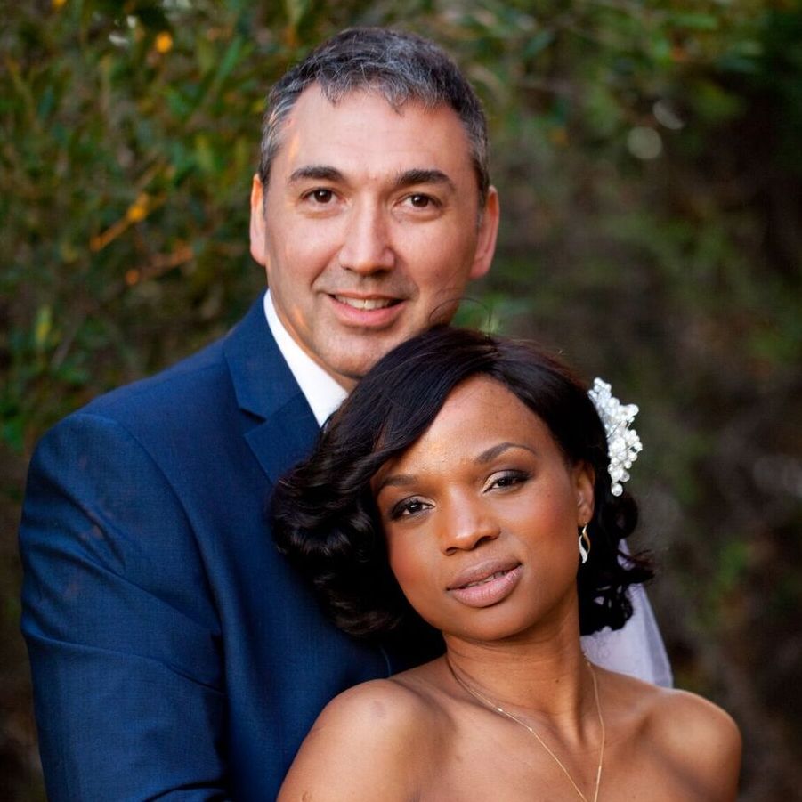 A man and woman are posing for a picture and the woman has a flower in her hair