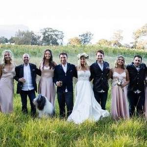 A bride and groom are posing for a picture with their wedding party in a field.