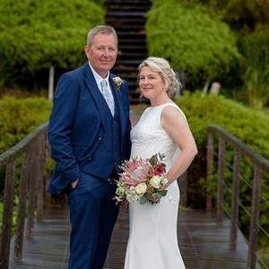 A bride and groom are posing for a picture on a wooden bridge.