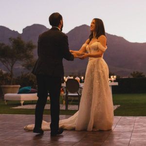 A bride and groom are holding hands in front of mountains