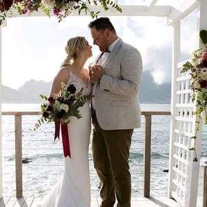 A bride and groom are kissing under a pergola overlooking the ocean.