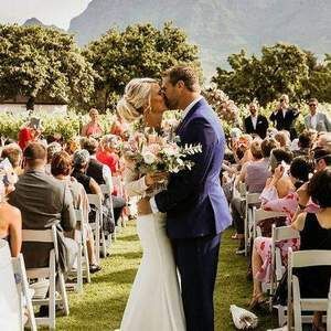 A bride and groom kissing at their wedding ceremony in front of a crowd of people.