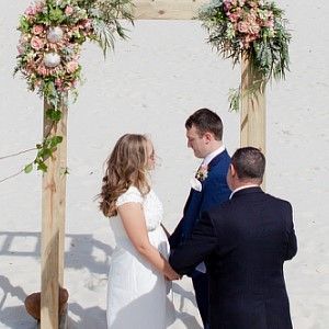 A bride and groom are holding hands during their wedding ceremony under a wooden arch.