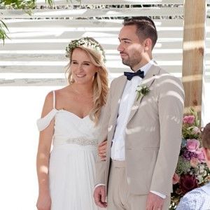A bride and groom are posing for a picture at their wedding . the bride is wearing a flower crown.