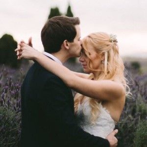 A bride and groom are kissing in a field of purple flowers.