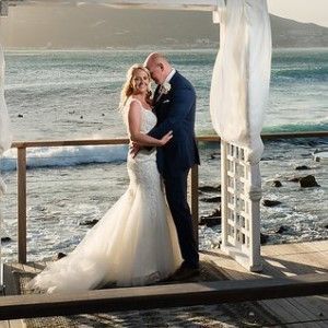 A bride and groom are posing for a picture on the beach.