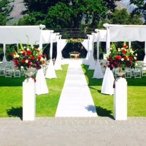 A white aisle is lined with white chairs and flowers