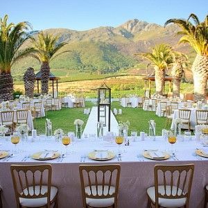 A long table with a view of mountains and palm trees is set up for a wedding reception.