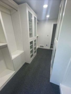 White custom closet with glass-front cabinets and built-in bench. Dark gray carpet and white walls.