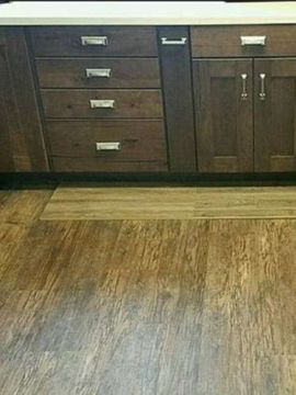 Wooden kitchen cabinets and drawers with silver handles, above wood-look flooring.
