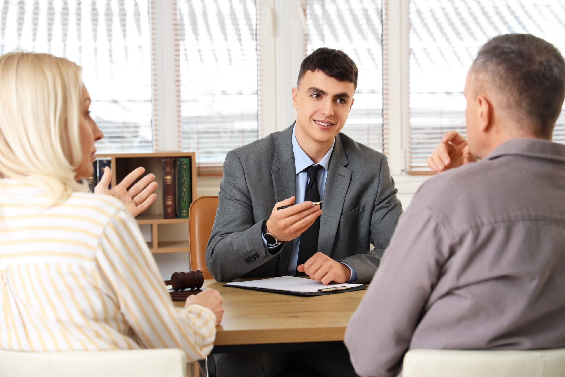 An attorney in a gray suit discusses legal matters with a couple seated across a desk with a gavel An attorney in a gray suit discusses legal matters with a couple seated across a desk with a gavel
