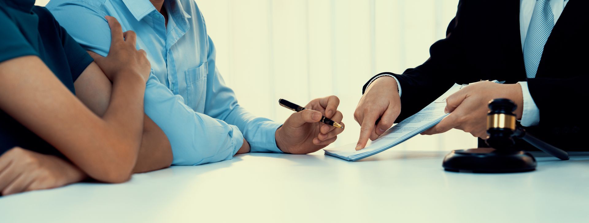 A legal consultation with two clients on the left and a lawyer on the right pointing at a document. A legal consultation with two clients on the left and a lawyer on the right pointing at a document.