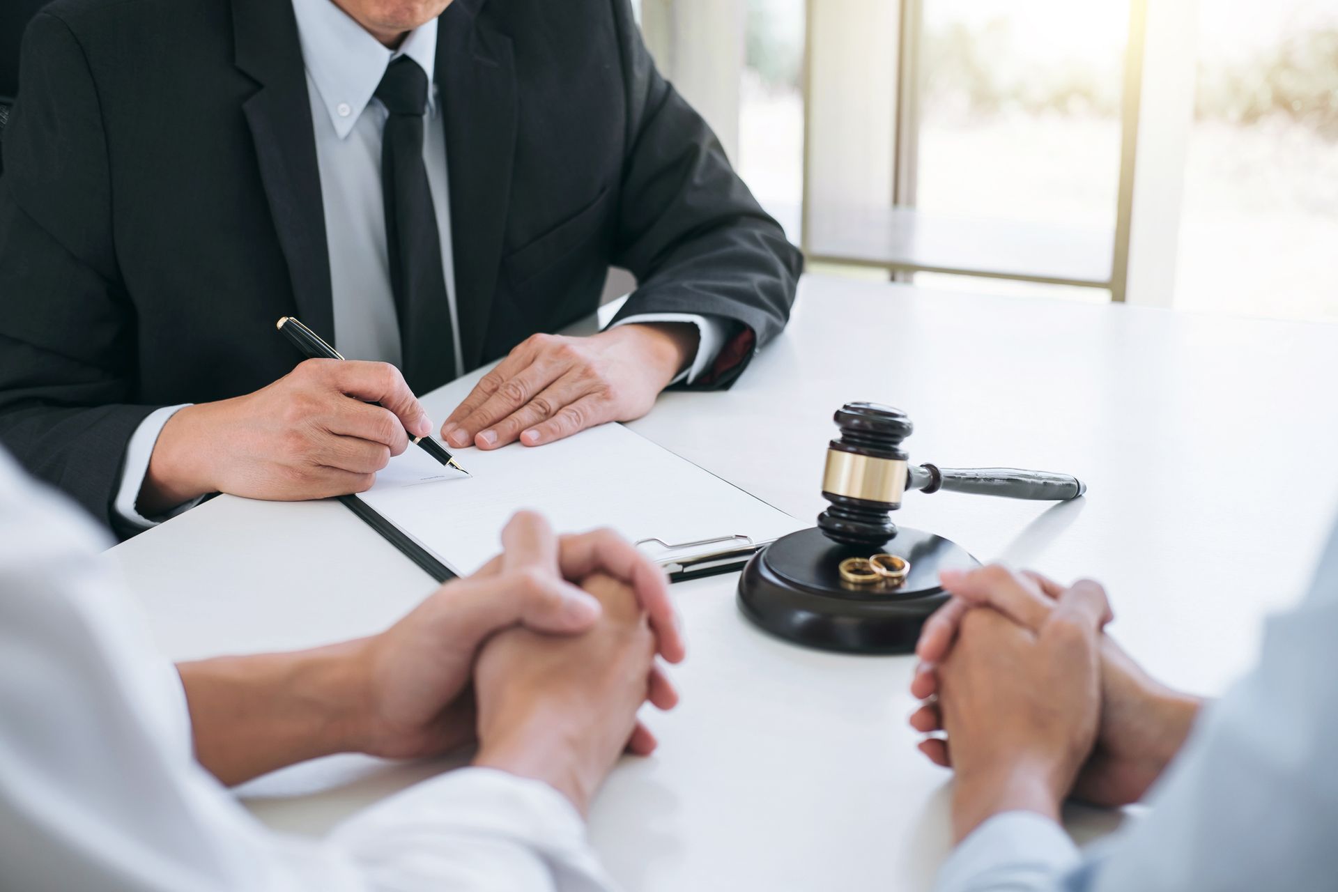 Lawyer signing document with clients; gavel on desk.
