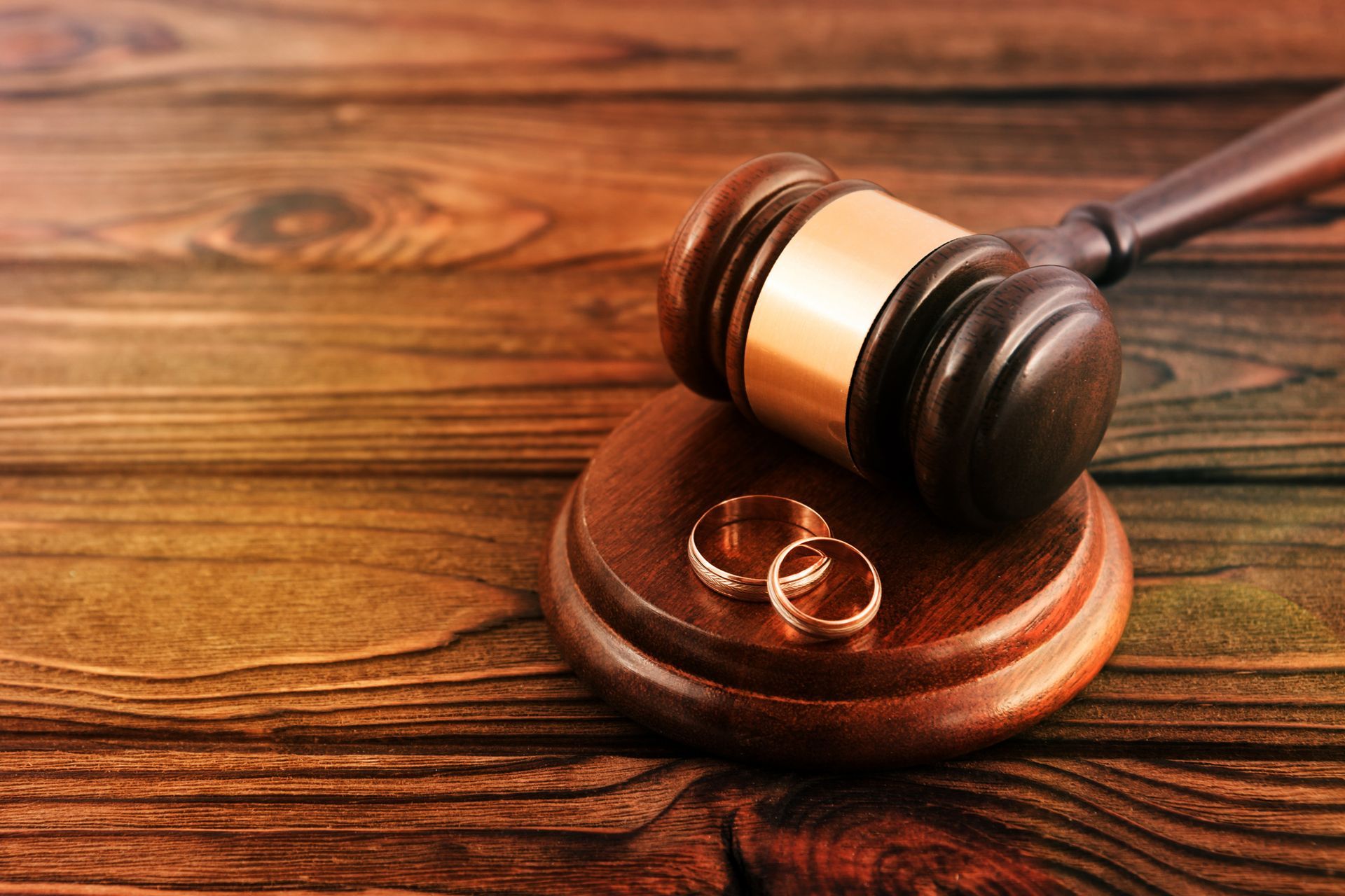 Wedding rings on a wooden stand next to a gavel, symbolizing divorce.