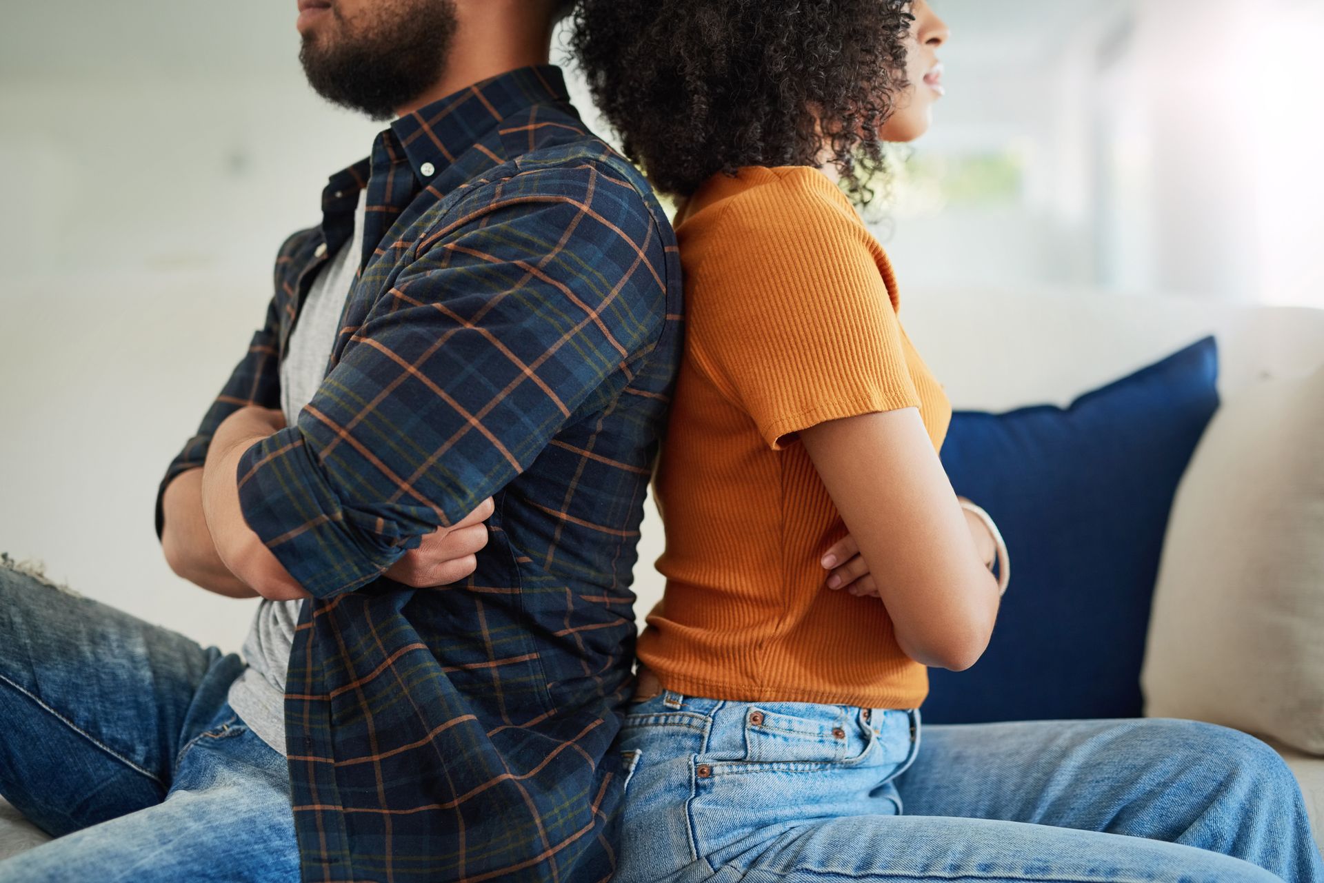 Couple sitting back to back with arms crossed, appearing upset.