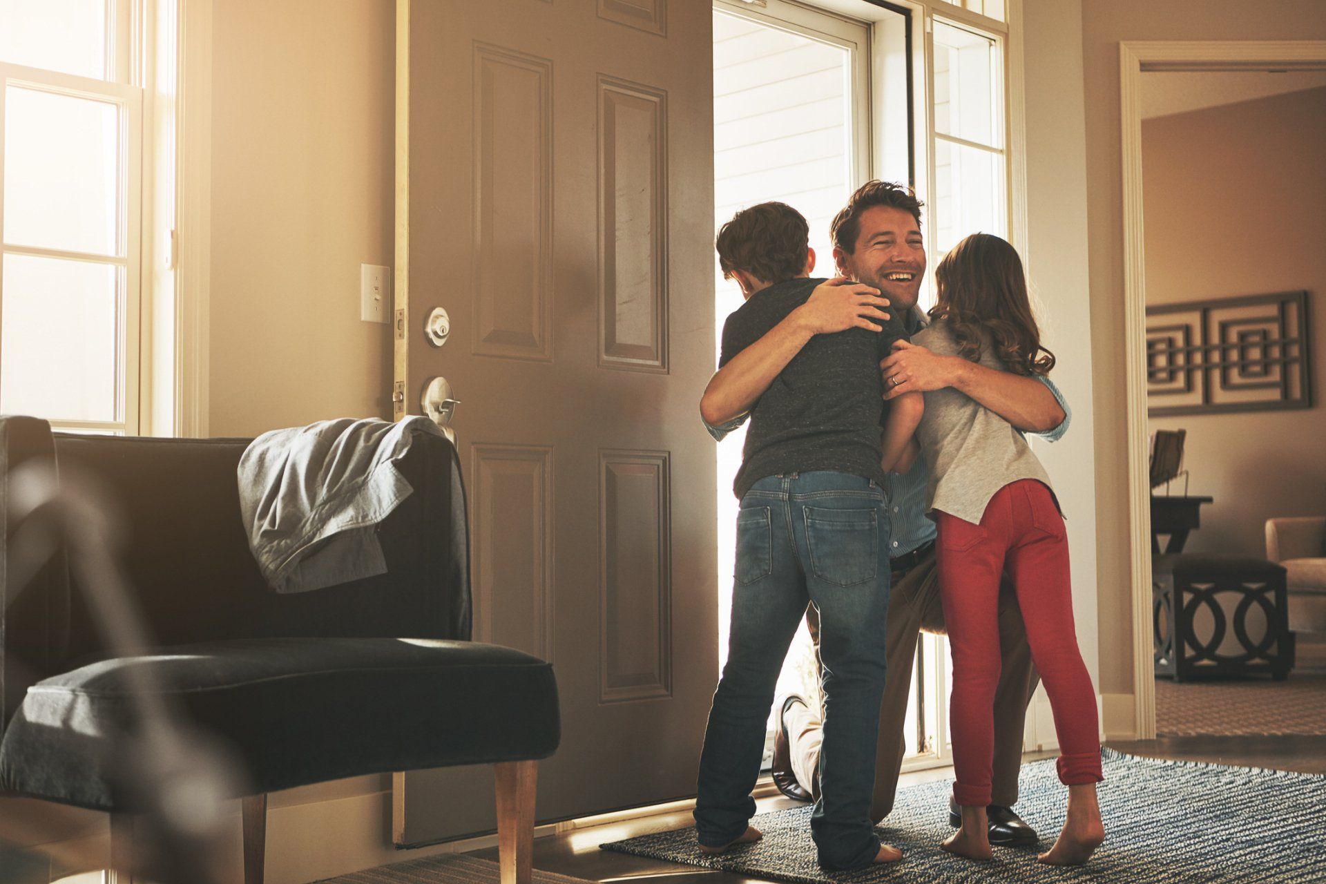 Father hugging two children in the doorway of a home. Sunlight streams in.