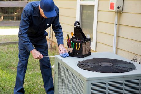 A man is working on an air conditioner outside of a house. A man is working on an air conditioner outside of a house.