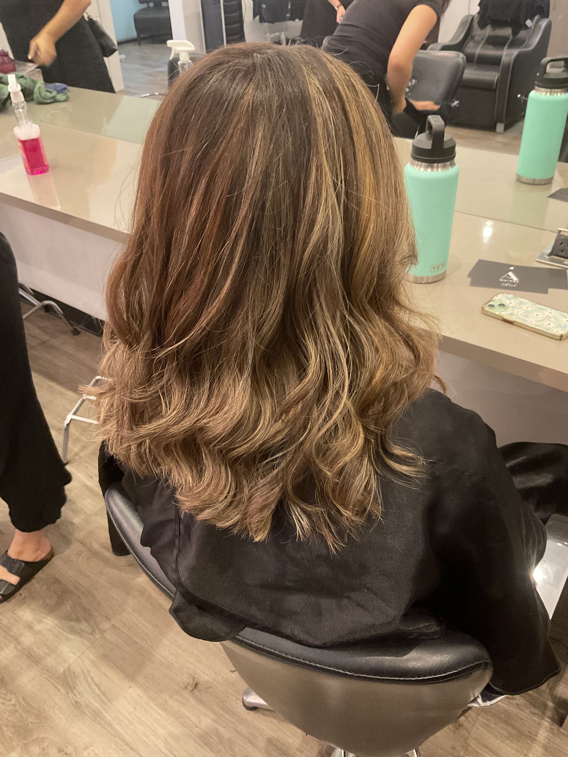 Woman Sitting in Front of a Mirror With a Hairstylist Working on Curls — Artistry Of Hair in Redlynch, QLD