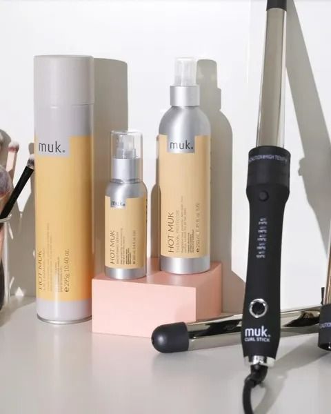 Hair Styling Products and a Curling Iron on a White Surface With a Pink Block — Artistry Of Hair in Redlynch, QLD