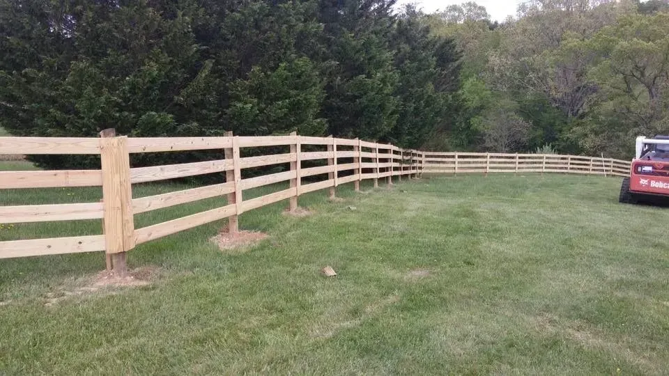 Wooden split-rail fence along a grassy lawn with trees in the background and a red car at right.