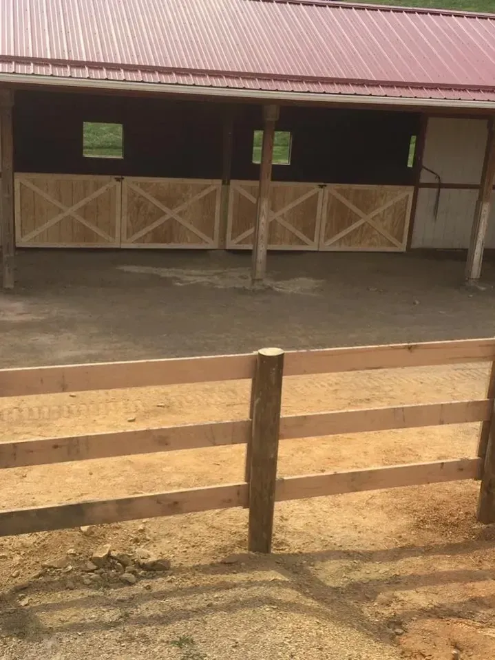Wooden fence in front of a rustic barn with a red roof and dirt ground