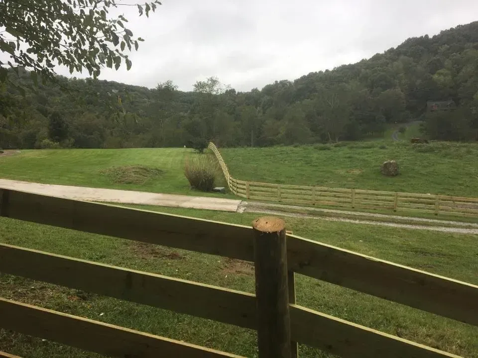 Wooden fence overlooking a green hillside and field with steps under an overcast sky