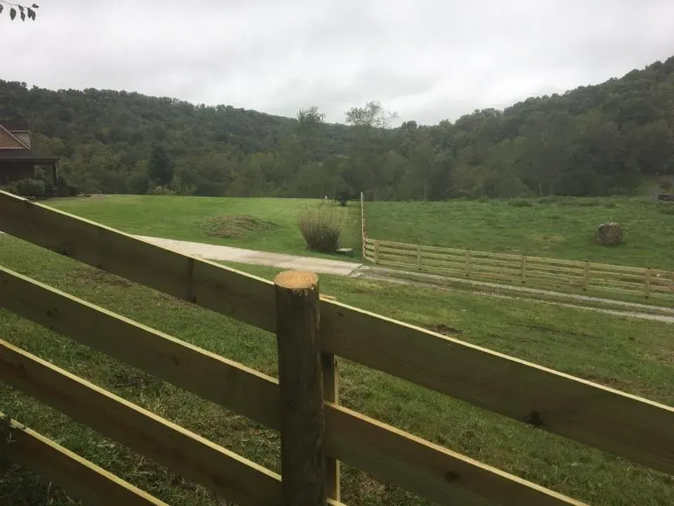 Wooden fence overlooking a green pasture and wooded hills under an overcast sky
