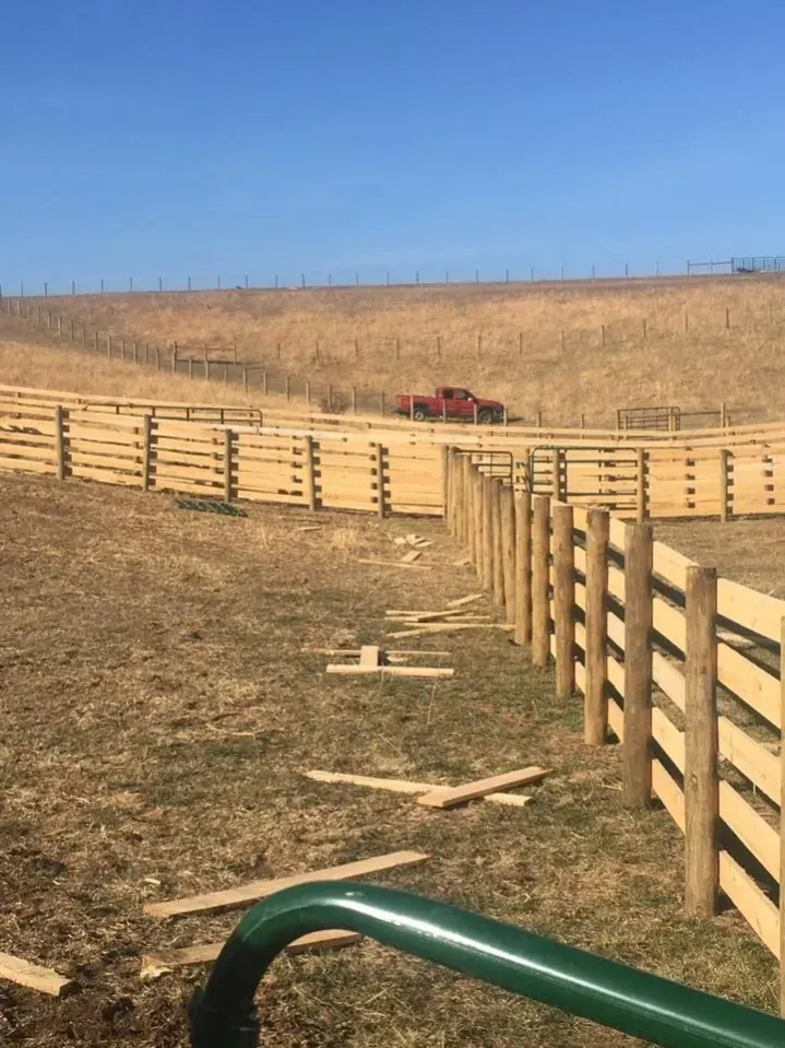 Horse paddock with wooden fencing on a dry hillside under a clear blue sky, red truck in the distance