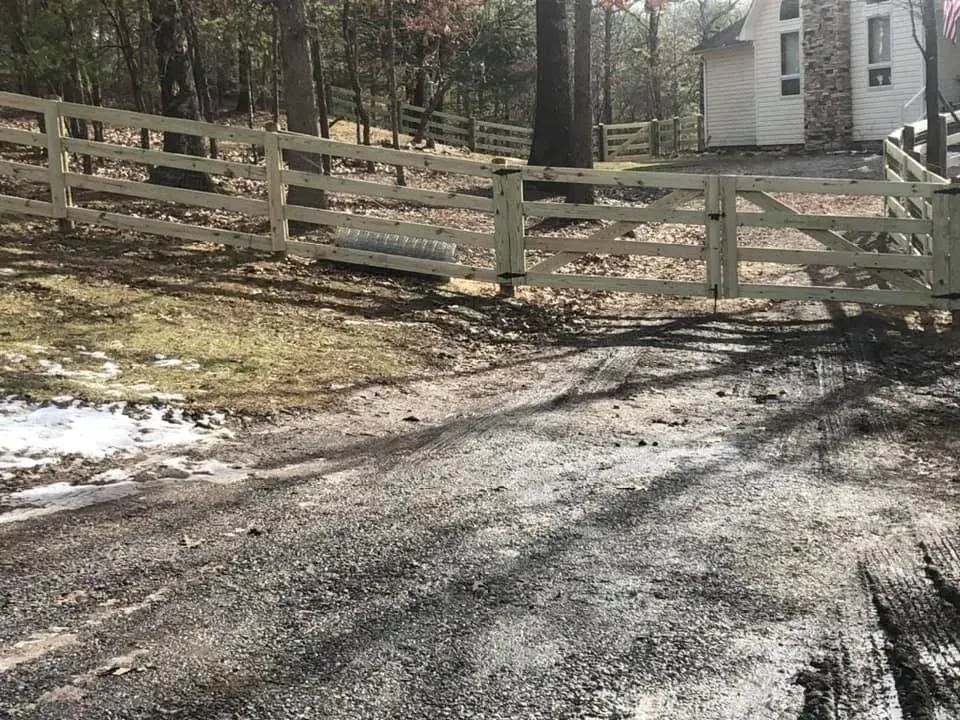 Gravel driveway beside a wooden fence and trees, leading to a small white cabin in the woods.