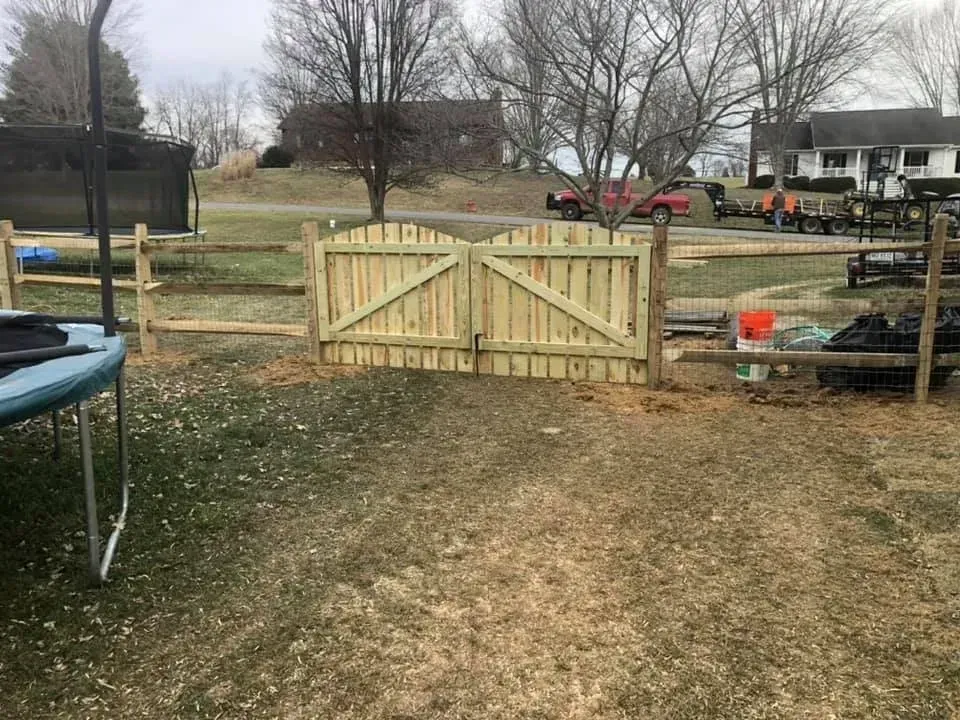 Wooden double gate at the end of a grassy backyard path, with trees and a house in the background.