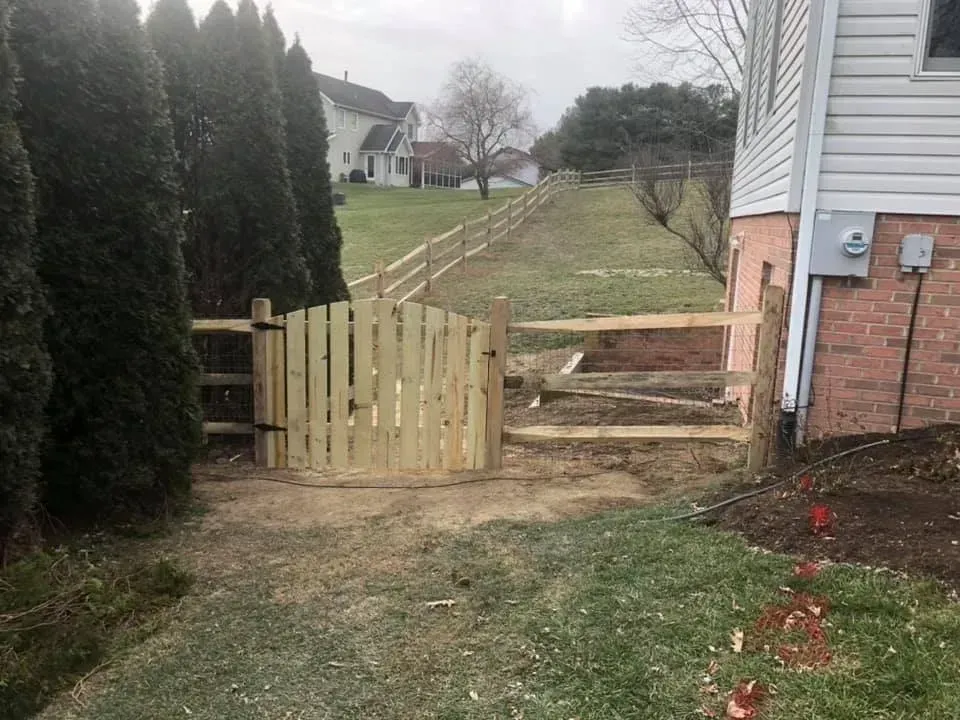 Backyard gate beside a house, opening to a sloped grassy path and steps leading uphill