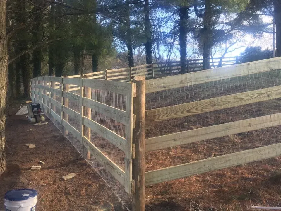 Long white wooden fence along a wooded dirt path with a bucket in the foreground