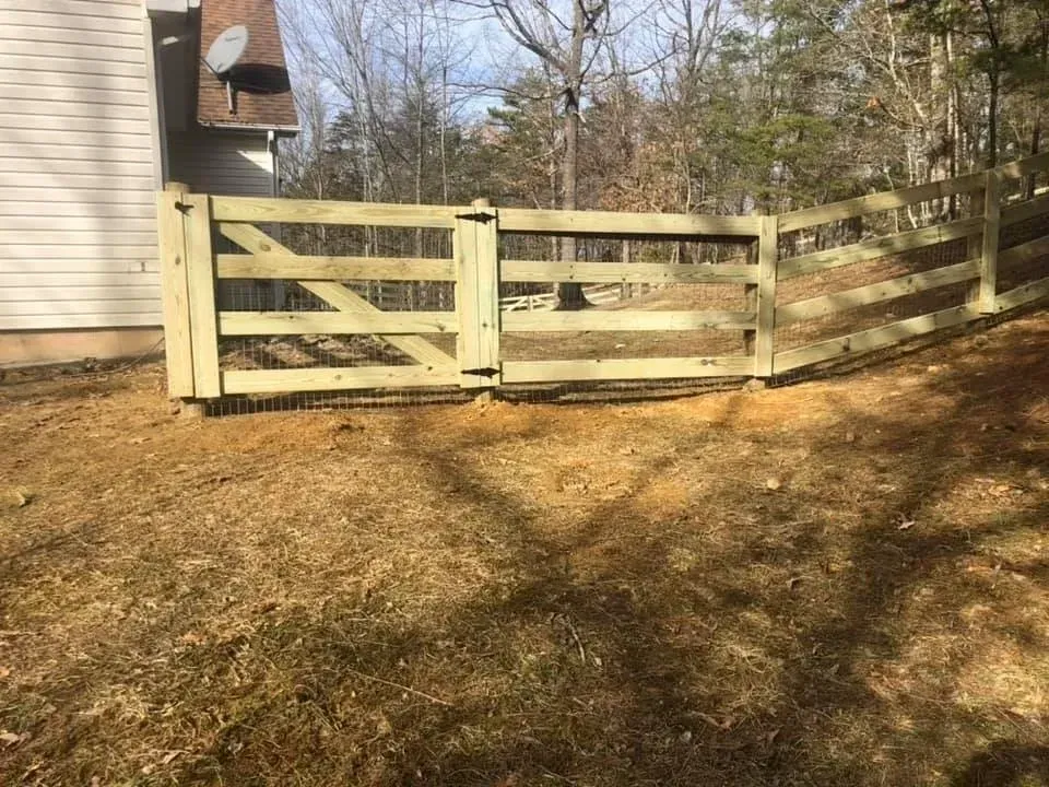 Wooden fenced walkway and gate on a sloped backyard beside a beige house