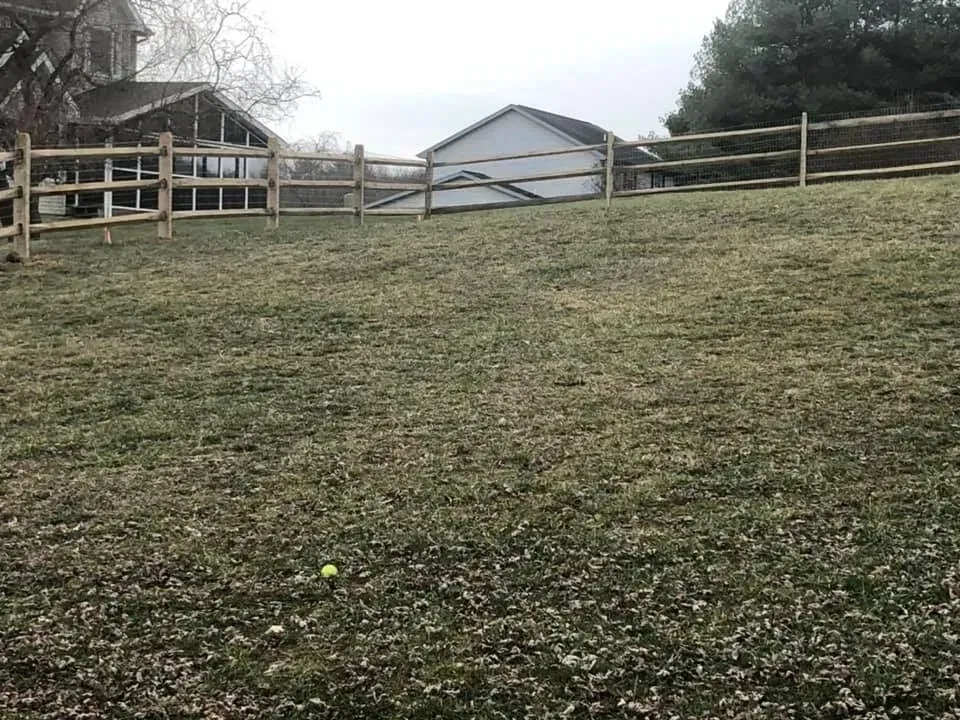 Grassy hill with a wooden fence and small barn in the distance under an overcast sky