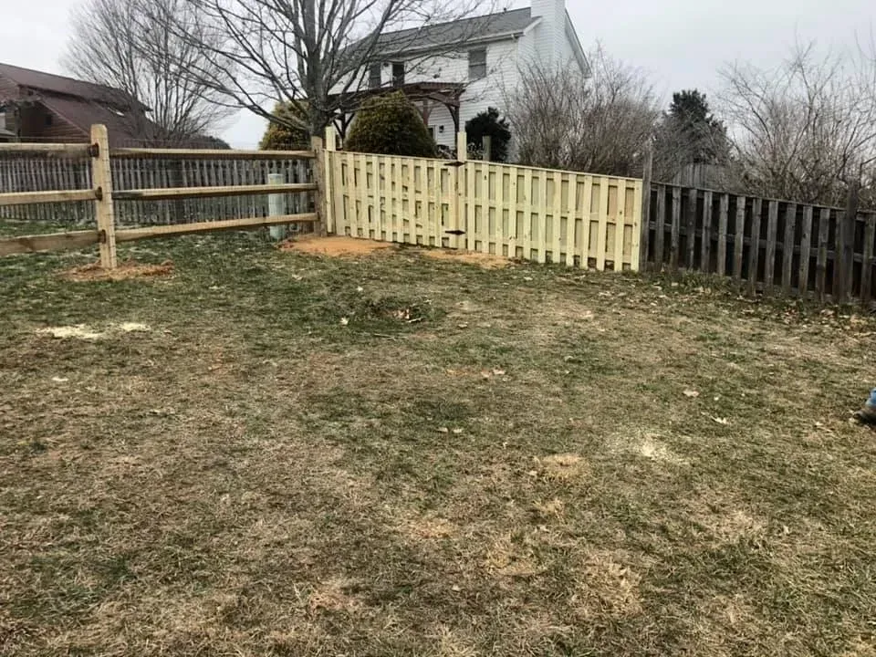 Backyard with three different fences and a small white house in the background