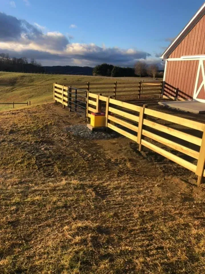 Sunlit rural fence beside a red barn under a cloudy sky