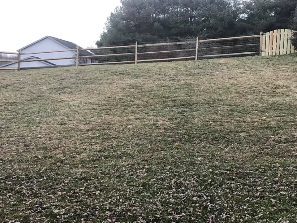Grassy hill with a wooden fence, trees, and a small white building in the background.