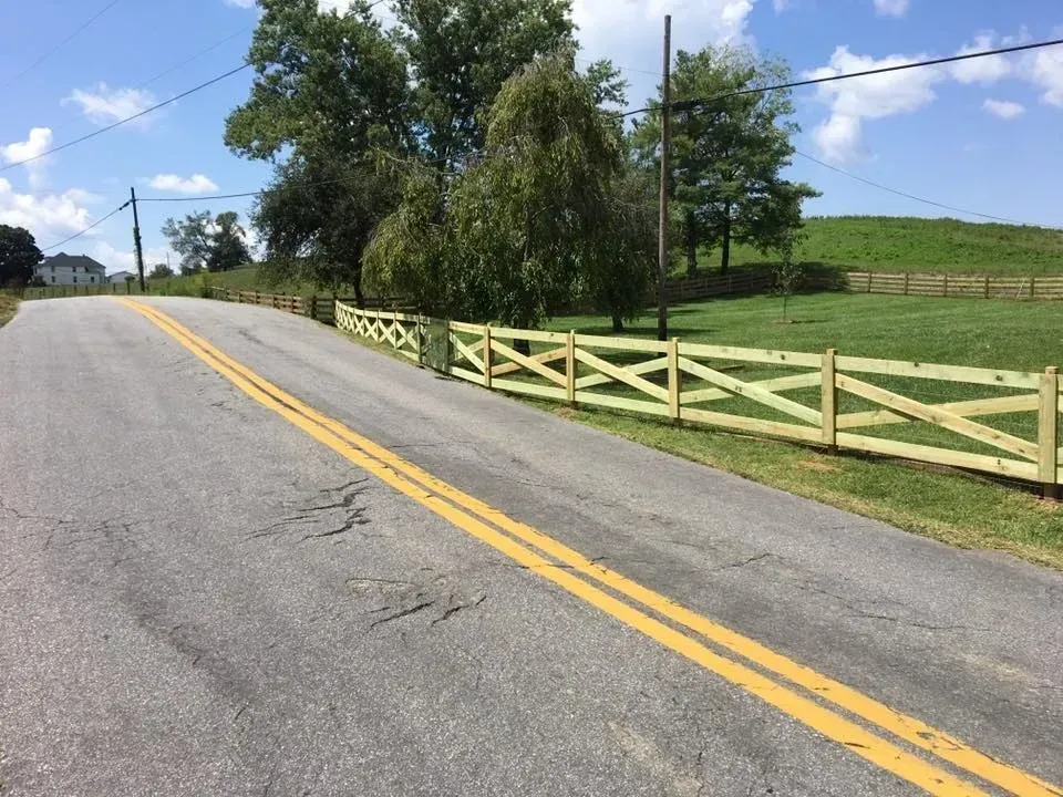 Curving country road with double yellow lines, wooden fence, and green fields under a blue sky