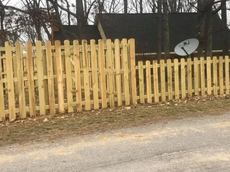 Weathered wooden fence beside a gravel road with a house and satellite dish in the background