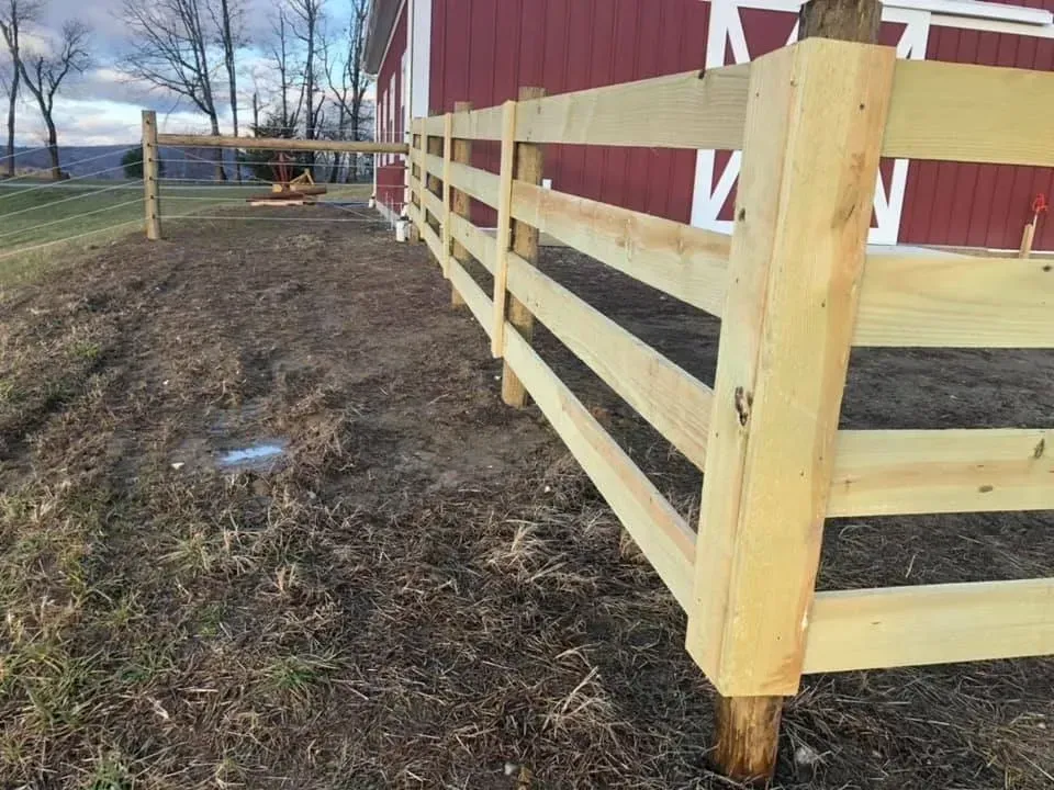 Fresh wooden fence beside a red barn on muddy ground in a rural yard