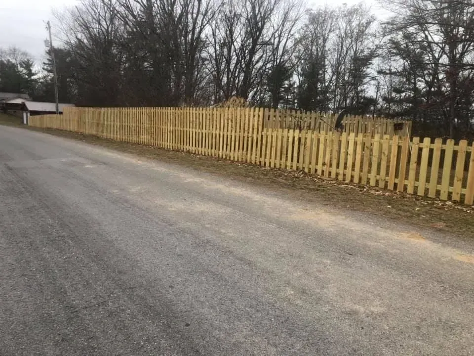 Gravel road beside a long yellow picket fence and leafless trees on a cloudy day