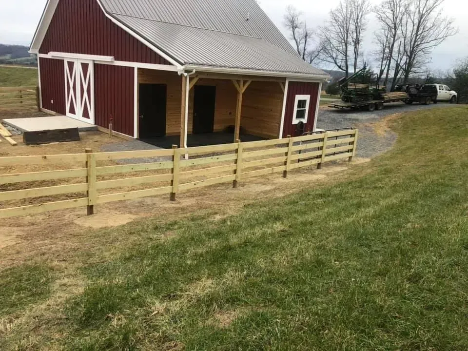 Red barn with white trim beside a fenced grassy field on a rural hillside
