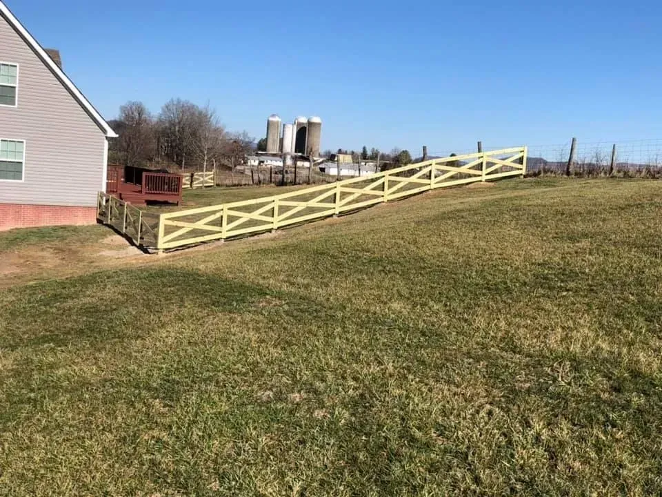 Yellow wooden ramp beside a pink house on a grassy hillside under a clear blue sky