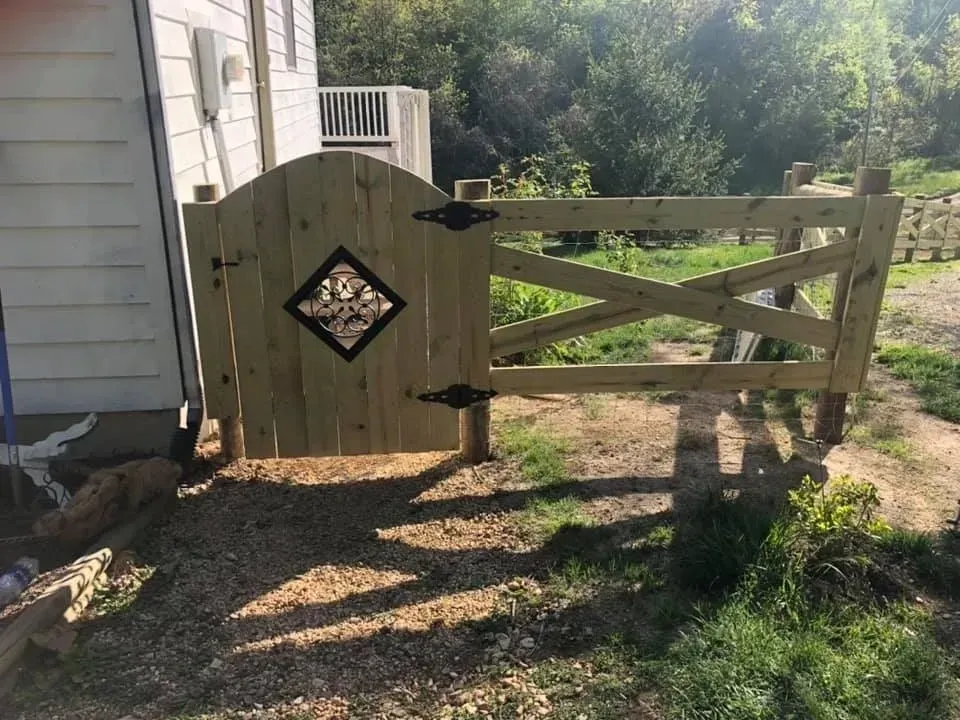 Wooden garden gate beside a house, with crisscross fence panels and gravel path.