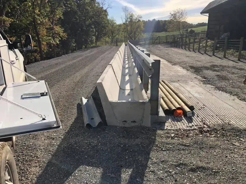 Roadside construction barrier beside a gravel lane, with pipes and equipment on the right.