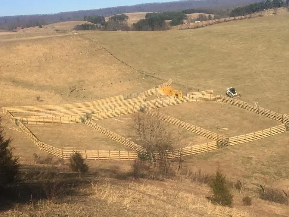 Fenced dirt arena on a dry hillside with a small orange structure and a parked white vehicle