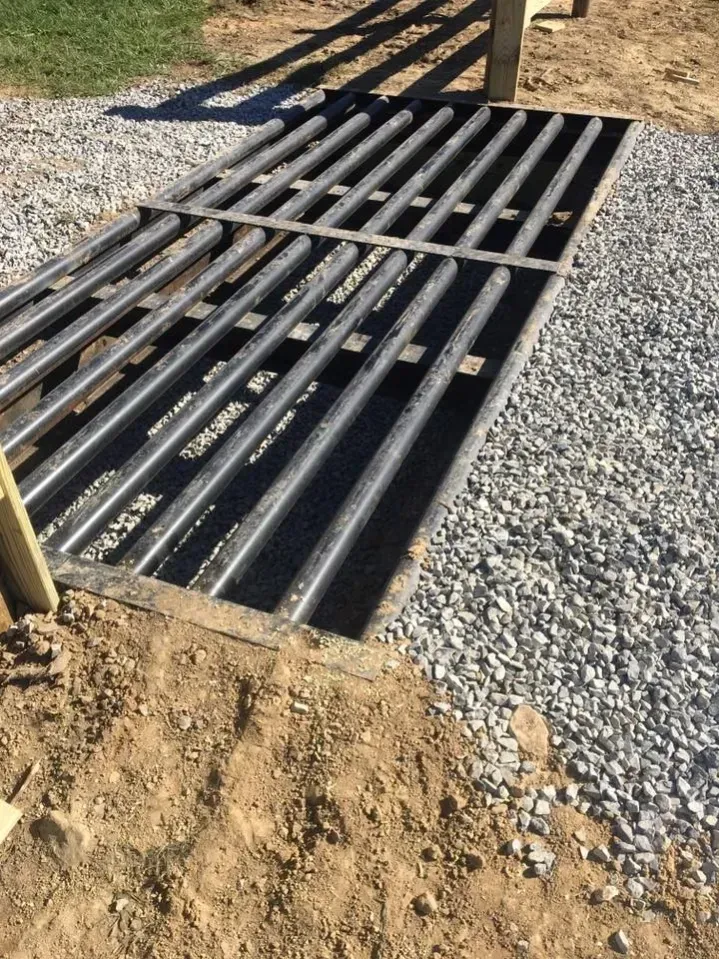 Metal drainage grate set in gravel and dirt at a construction site